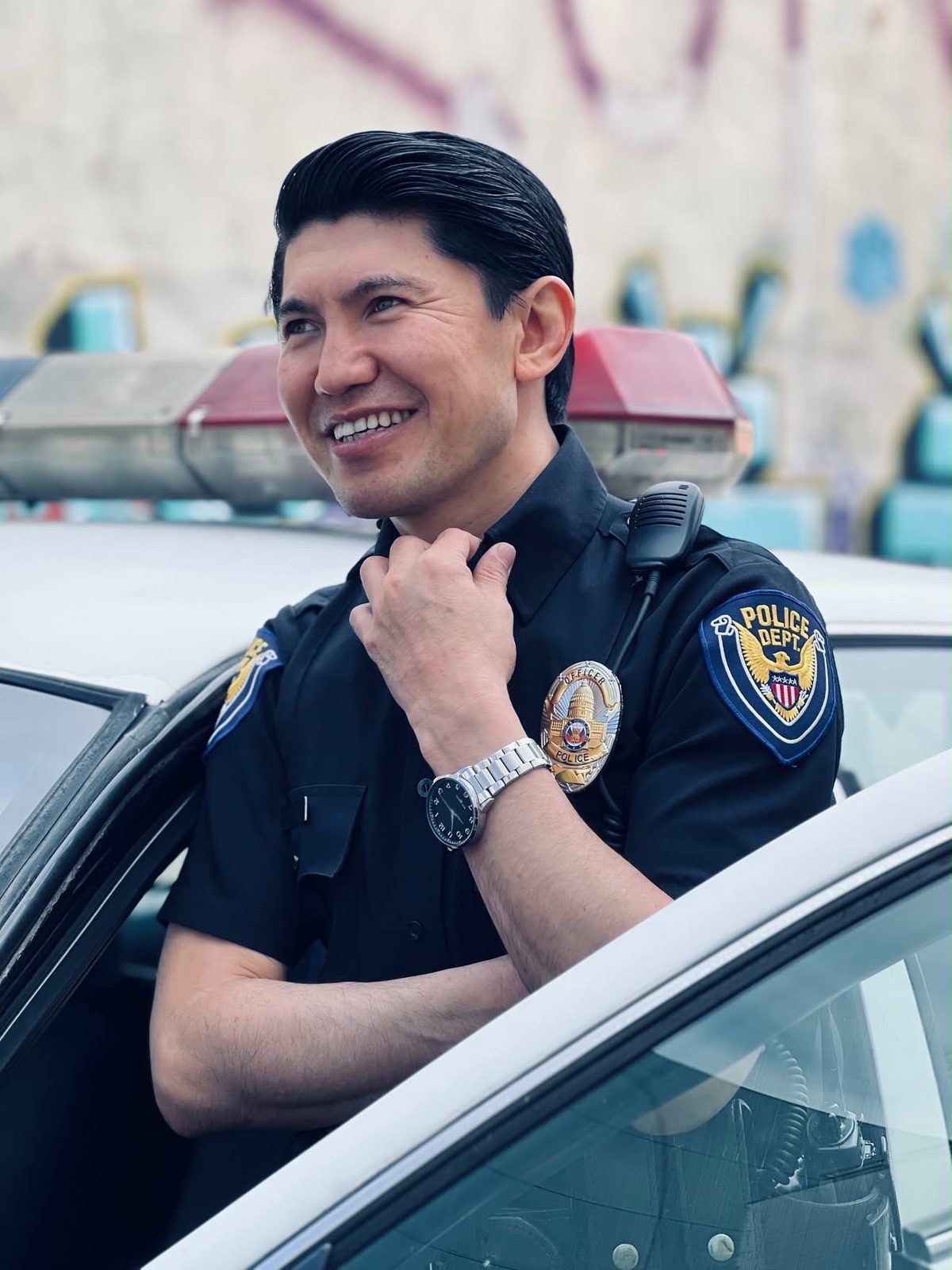 Medet Aman in uniform, smiling and leaning on a patrol car